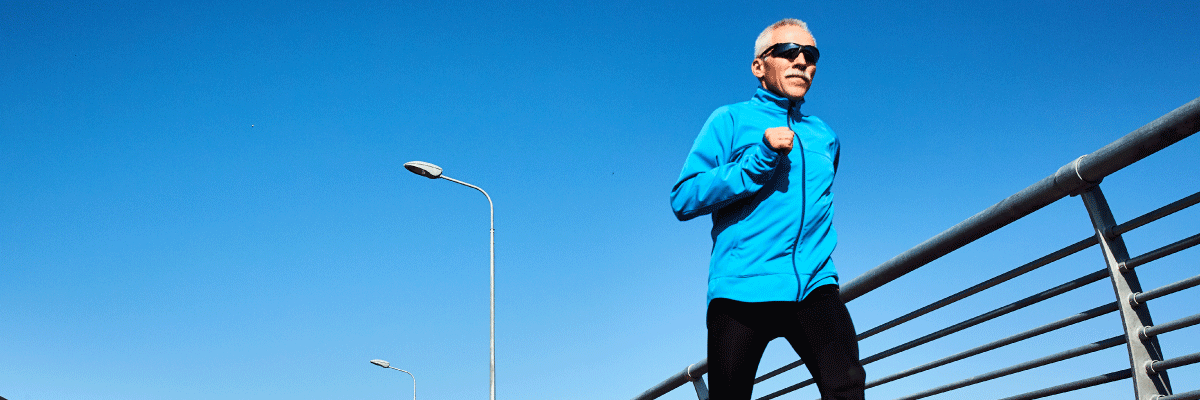 Man in a blue jacket running on a bridge with clear blue sky