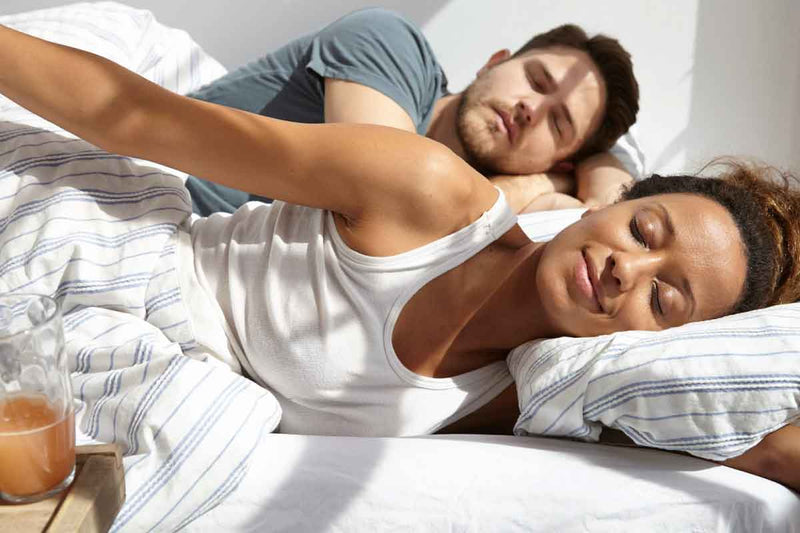 Two people lying in bed with a glass of IN DREAM on a nightstand.
